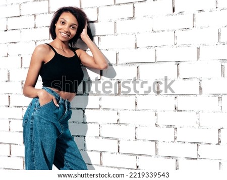 Portrait of young beautiful black woman. Smiling model dressed in summer jeans clothes. carefree female posing near white brick wall in studio. Tanned and cheerful