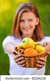 portrait of young beautiful blond smiling woman holding a basket with fresh juicy fruits in summer green park