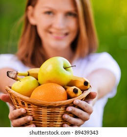 portrait of young beautiful blond smiling woman holding a basket with fresh juicy fruits in summer green park