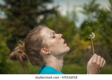 Portrait of young beautiful blonde blowing on a dandelion