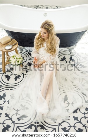 portrait of a young beautiful blonde bride with a bottle of champagne in the bathroom