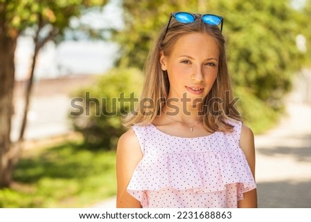 Portrait of a young beautiful blonde girl in pink dress, summer park outdoors