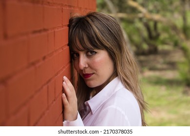 Portrait Of Young, Beautiful, Blonde Woman In White Shirt With Her Face Leaning Against A Red Brick Wall, With Flirtatious Look. Concept Beauty, Fashion, Desire, Lust.