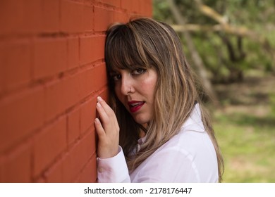 Portrait Of Young, Beautiful, Blonde Woman In White Shirt With Her Face Leaning Against A Red Brick Wall, With Flirtatious Look. Concept Beauty, Fashion, Desire, Lust.