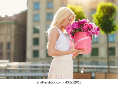 Portrait of young beautiful blonde woman with box of flowers posing in the city streets. flower box and gift box. bouquet of flowers in gift box. birthday, March 8, Valentine's Day, romantic
