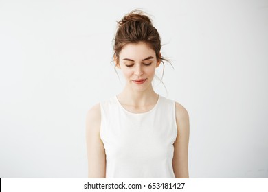 Portrait of young beautiful brunette girl smiling looking down over white background.