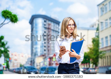 Portrait of a young beautiful business girl in glasses walking on summer street