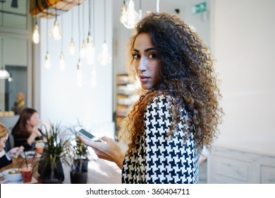 Portrait of a young beautiful businesswoman sending text message from her digital smart-phone in coffee-shop