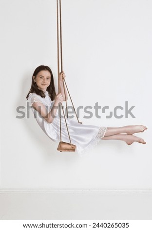Portrait of young beautiful caucasian girl in white dress swinging on the white background