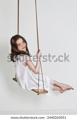 Portrait of young beautiful caucasian girl in white dress swinging on the white background