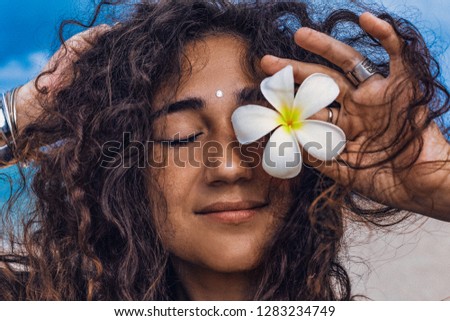 Portrait of young and beautiful cheerful woman with frangipani flower on the beach 
