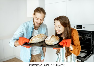 Portrait of a young beautiful couple holding tray with fresh baked breads in the modern bright kitchen at home - Powered by Shutterstock