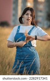 Portrait of a young beautiful dark-haired girl in a denim sundress on a summer field.