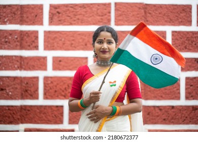 Portrait of a young beautiful female holding the Indian flag on national celebration Republic day India against a red brick wall - Shutterstock ID 2180672377