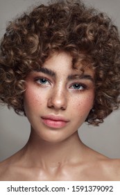 Portrait of young beautiful freckled girl with curly hair and clean makeup