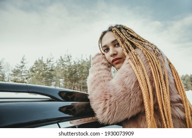 Portrait of a young beautiful girl with box braids hairstyle  next to a car in winter nature. Girl posing for social media.