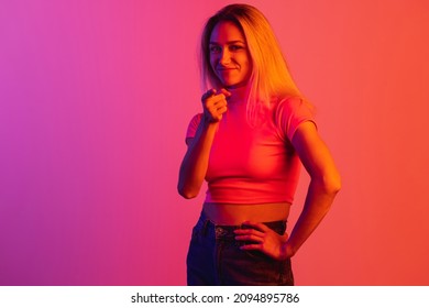 Portrait of young beautiful girl with grinning face pointing at camera isolated over gradient background in neon lights. Concept of human emotions, facial expression, beauty. Copy space for ad