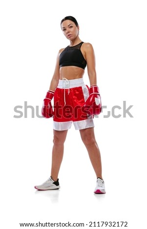 Portrait of young beautiful girl, professional boxer in boxing shorts and gloves posing isolated on white studio background. Sport, competition, show, power, action concept.