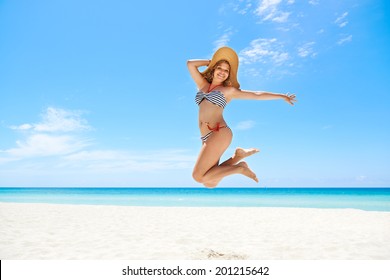 Portrait of young beautiful girl at tropical beach for vacations, jumping mid-air for joy, looking at camera and smiling. Copy space
