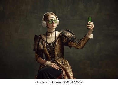 Portrait of young beautiful girl in vintage dress, trendy sunglasses and headphones, taking selfie with phone against dark green background. Concept of history, renaissance art, comparison of eras