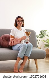 Portrait Of Young Beautiful Hipster Woman With Her Adorable Four Months Old Jack Russell Terrier Puppy At Home In Living Room Full Of Natural Sunlight. Lofty Interior Background, Close Up, Copy Space.