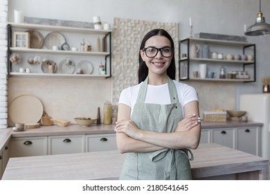 Portrait Of Young Beautiful Housewife In Dressing Gown Apron, Woman With Crossed Arms Smiling And Looking At Camera, In Kitchen