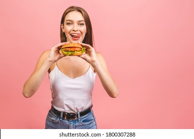 Portrait Of Young Beautiful Hungry Woman Eating Burger. Isolated Portrait Of Student With Fast Food Over Pink Background. Diet Concept. 