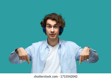 Portrait Of A Young Beautiful Man Wearing White T-shirt And Blue Shirt In Headphones. Point To Something Down Or Somebody By His Forefingers