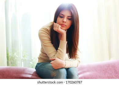 Portrait of a young beautiful pensive woman sitting on sofa at home