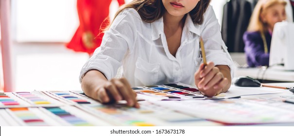 Portrait of young beautiful pretty woman fashion designer stylish sitting and working with color samples.Attractive young girl working with mannequins standing and colorful fabrics at fashion studio