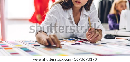 Portrait of young beautiful pretty woman fashion designer stylish sitting and working with color samples.Attractive young girl working with mannequins standing and colorful fabrics at fashion studio
