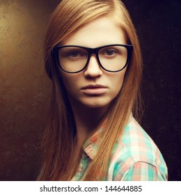 Portrait Of A Young Beautiful Red-haired Student Girl Wearing Trendy Glasses And Casual Shirt And Posing Over Golden Background. Hipster Style. Close Up. Studio Shot