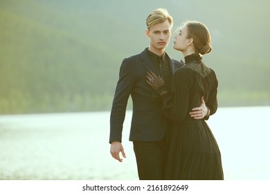 Portrait Of Young Beautiful Romantic Couple In Black Elegant Clothes Standing By The Sea And Hugging Each Other. Historical Romance Novel. 19th Century.