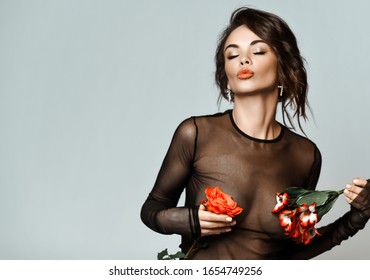 Portrait of young beautiful sexy brunette woman in black transparent clothing holding flowers on nipples places over grey background. Beauty, fashion, style concept