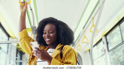 Portrait of young beautiful smiling african american girl using her cell phone in public transportation.