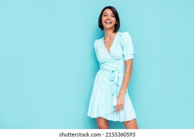 Portrait of young beautiful smiling female in trendy summer dress. Carefree woman posing near blue wall in studio. Positive model having fun indoors. Cheerful and happy. Isolated