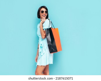 Portrait of young beautiful smiling female in trendy summer dress. Carefree woman posing near blue wall in studio. Positive model holding shopping bag. Cheerful and happy. Isolated - Shutterstock ID 2187615071