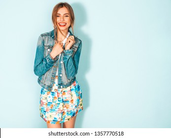 Portrait Of Young Beautiful Smiling Hipster Girl In Trendy Summer Jeans Jacket Clothes. Sexy Carefree Woman Posing Near Blue Wall. Positive Model Having Fun 