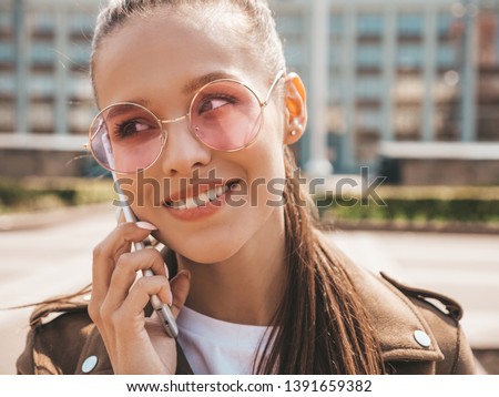 Portrait of young beautiful smiling woman speaking on phone. Trendy girl in casual summer clothes. Funny and positive female posing on the street background 