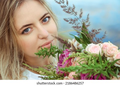 Portrait Of Young Beautiful Woman Caucasian Appearance Smiling And Looking At Camera Through The Lush Flowers Bouquet. Happy Summer Mood. Attractive Girl Lifestyle. Big Blue Lady Eyes. Flirting Look.