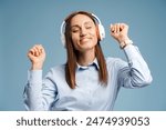 Portrait of young beautiful woman closing eyes wearing headphones and listening music on blue background, holding hands. Technology, lifestyle, people concept