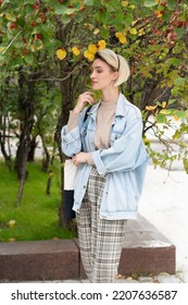 Portrait Of A Young Beautiful Woman In A Denim Jacket Outside, Stands Near A Green Bush