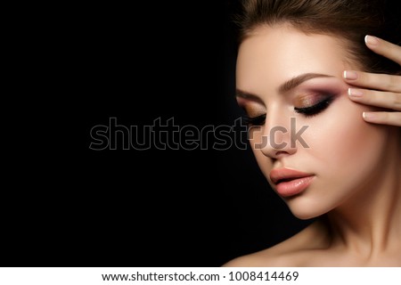 Portrait of young beautiful woman with evening make up touching her face over black background. Multicolored smokey eyes. Luxury skincare and modern fashion makeup concept. Studio shot. Copy space