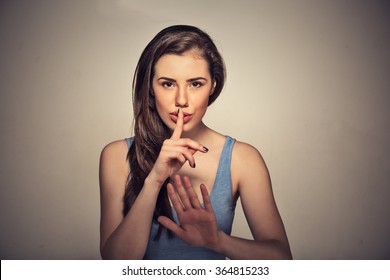 Portrait of young beautiful woman with finger on lips isolated on gray wall background