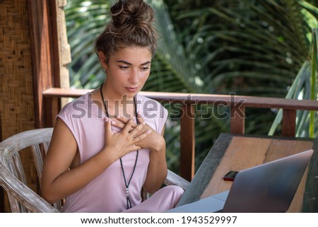Portrait of young beautiful woman freelancer working with laptop on balcony of tropical bungalow with palm trees view in Bali