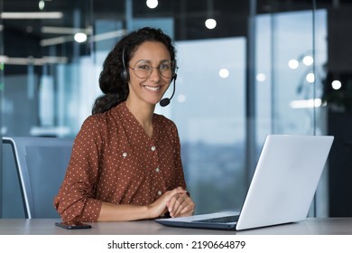 Portrait of young beautiful woman in glasses, looking at camera and smiling Arab woman using headset and laptop for video call, working in modern office, customer support service - Shutterstock ID 2190664879