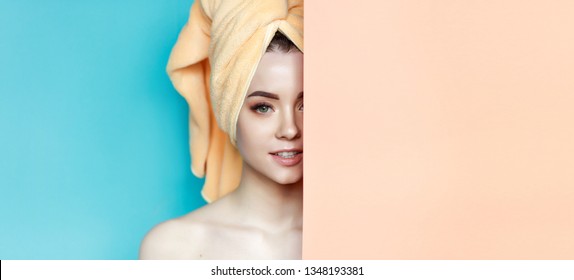 Portrait Of Young Beautiful Woman With Healthy Glow Perfect Smooth Skin Look Into The Hole Of Blue And Orang Paper. Model With Natural Nude Make Up With Towel On Head. Fashion, Beauty, Skincare.