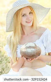 portrait of young beautiful woman holding fresh tasty bread in summer green park. soft focus
