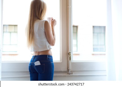Portrait of young beautiful woman at home with mobile phone in back pocket.