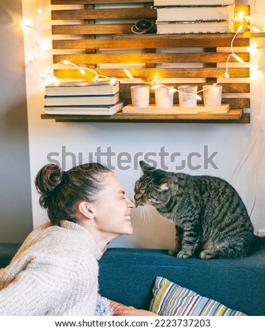 Portrait of a young beautiful woman hugging kissing with a gray fluffy cat sitting on the sofa
